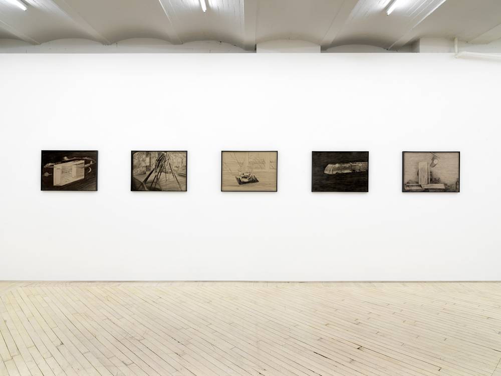 In a gallery space, a row of evenly spaced pencil drawings behind tinted glass frames. The frames are black. The drawings depict abstracted landscapes resembling constructed dream worlds.