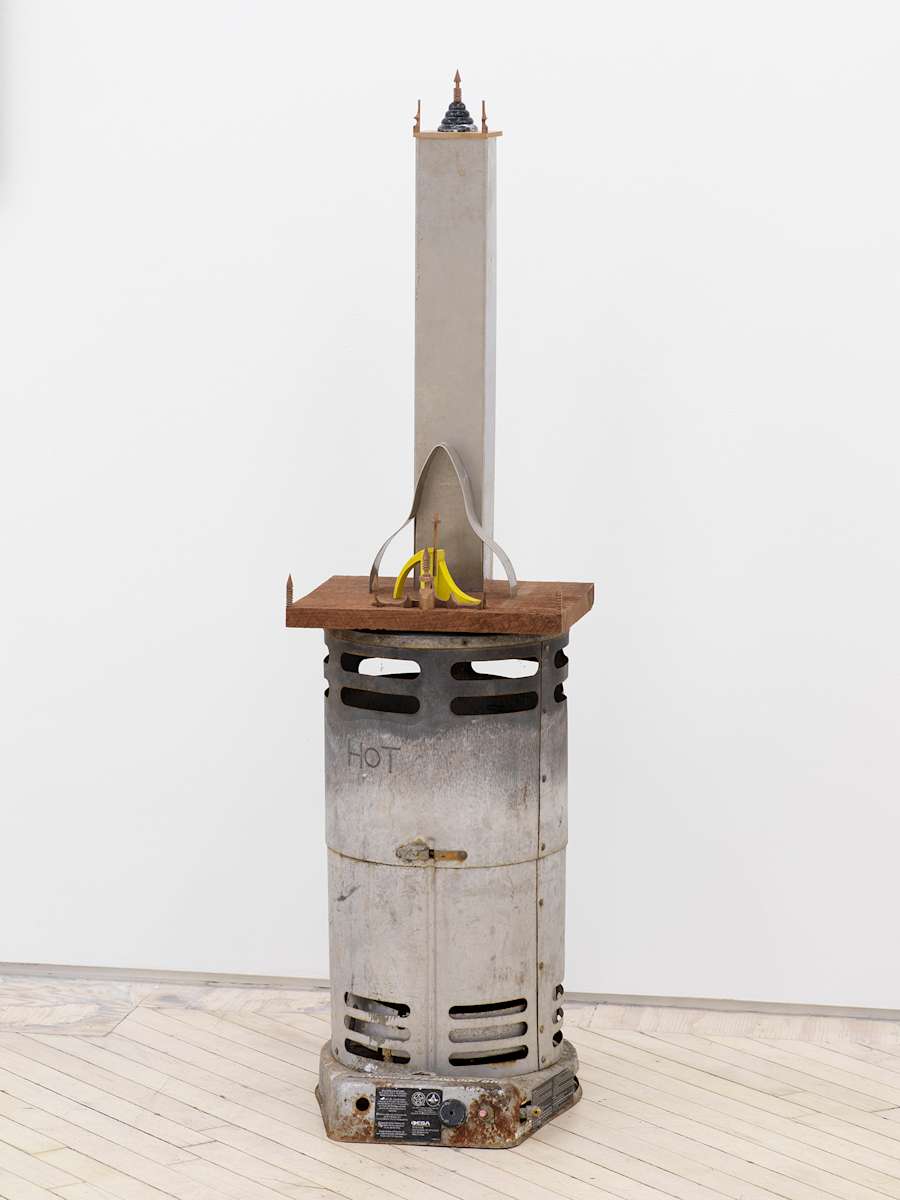 Image of Harry Gould Harvey IV sculpture made from a found metal kerosene heater, with a walnut platform on top containing a small yellow sculpture and a tower like form made of metal with another tier of small sculptures on top.