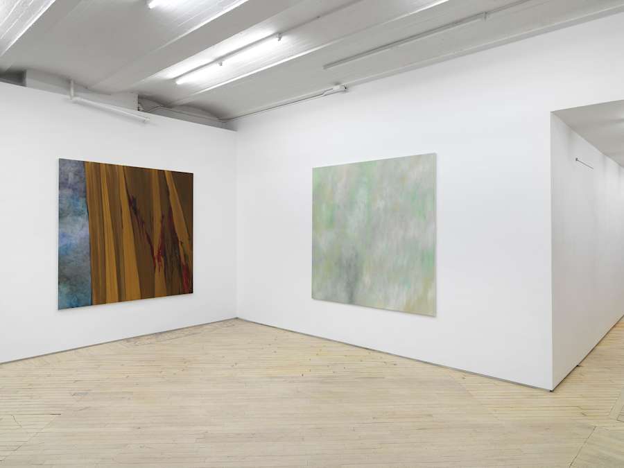 Two large, square abstract paintings are hung in the corner of a large gallery space.