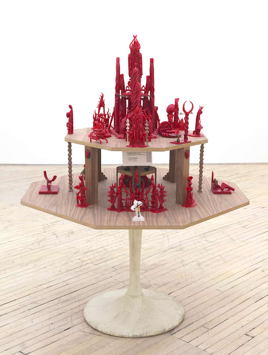 Installation view of Harry Gould Harvey IV sculpture made of smaller red wax sculptures resting on a tiered wooden platform on top of a tulip table base.