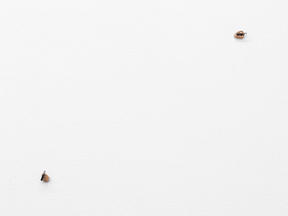 A white gallery wall with two miniature objects attached to it resembling technical equipment.