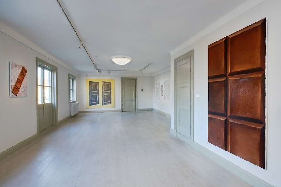 Installation view of the exhibition "Början och slut" at Fullersta Gård in Stockholm. On the left is a small diagonal chocolate painting, in the center is a painting of two doors next to each other, and in the foreground on the right size is a large cropped chocolate painting.