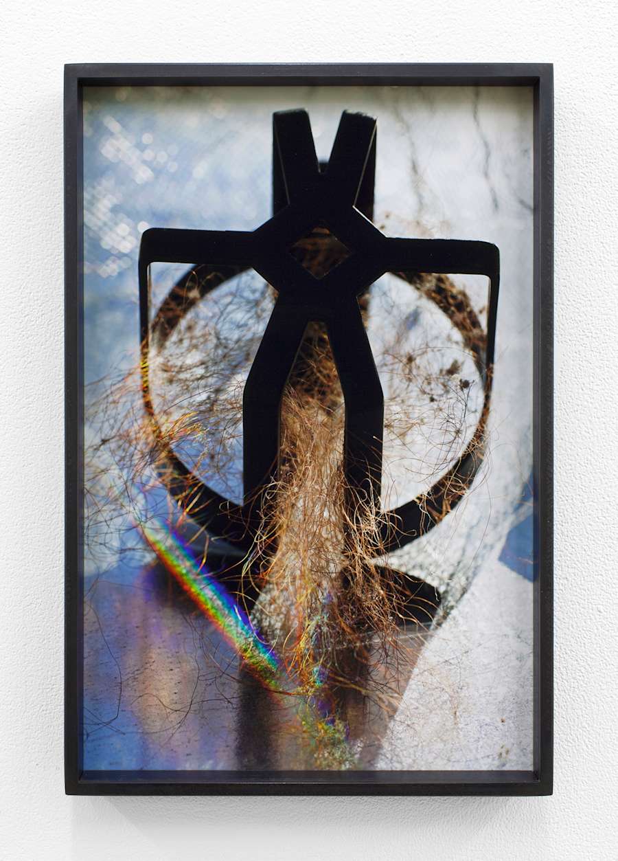 A round metal object, similar to a shower knob, is filled with strings of brown hair, a prism of like shines like a rainbow at the bottom left corner of the image.