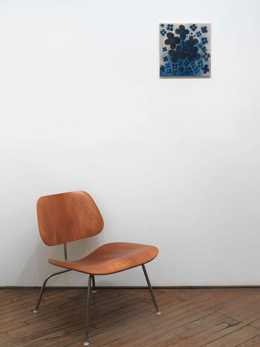 A small square abstract painting depicting graphic flowers in black and blue. Below is a chair.