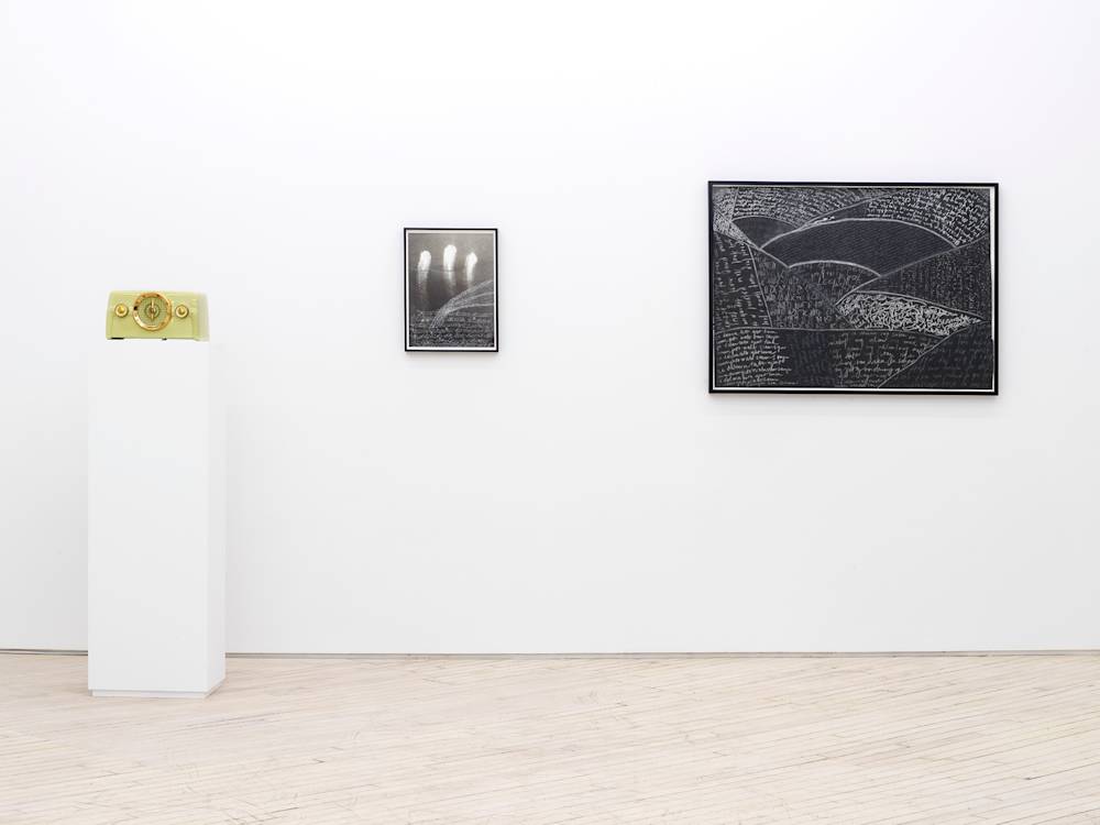 On the left, a green vintage radio on top of a pedestal. To the right are two framed artworks resembling black and white drawings or photographs. Both contain handwritten writing in white.