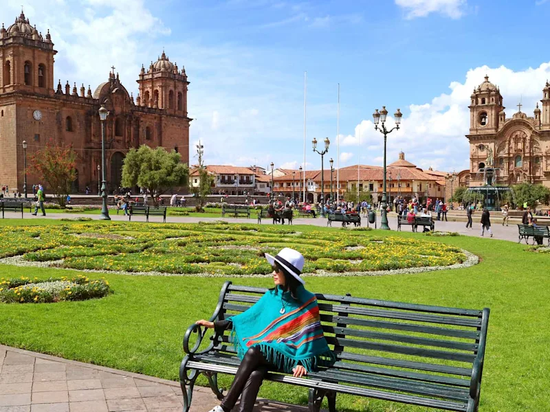 Female-relaxing-on-a-bench-at-Plaza-de-Armas-with-Cusco-Cathedral-and-the-Iglesia-de-la-Compania-de-Jesus-in-backg