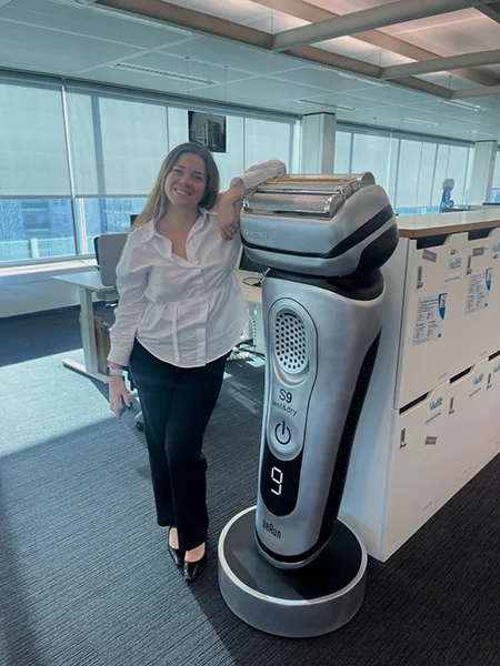 Mujer sonriendo junto a una gran exhibición de afeitadora eléctrica Braun en una oficina