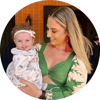 Una mujer de cabello largo y rubio, con un vestido verde, sosteniendo y mirando a su hija.