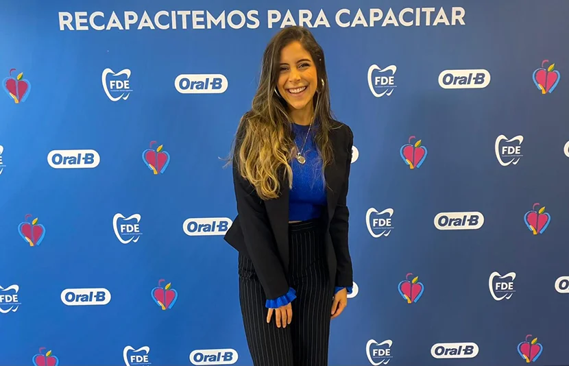 Mujer sonriendo con atuendo de negocios, de pie frente a un colorido fondo promocional