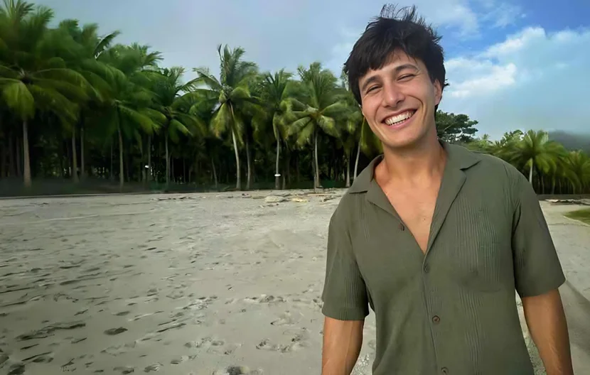 Joven sonriendo en una playa rodeado de palmeras y cielos azules