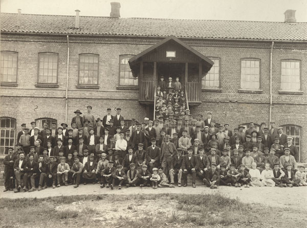 group portrait of a large number of people standing in front of a factory