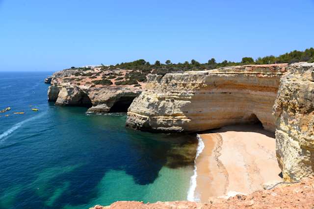 A small, enclosed beach under tall cliffs with clear blue water in Algarve, Portugal