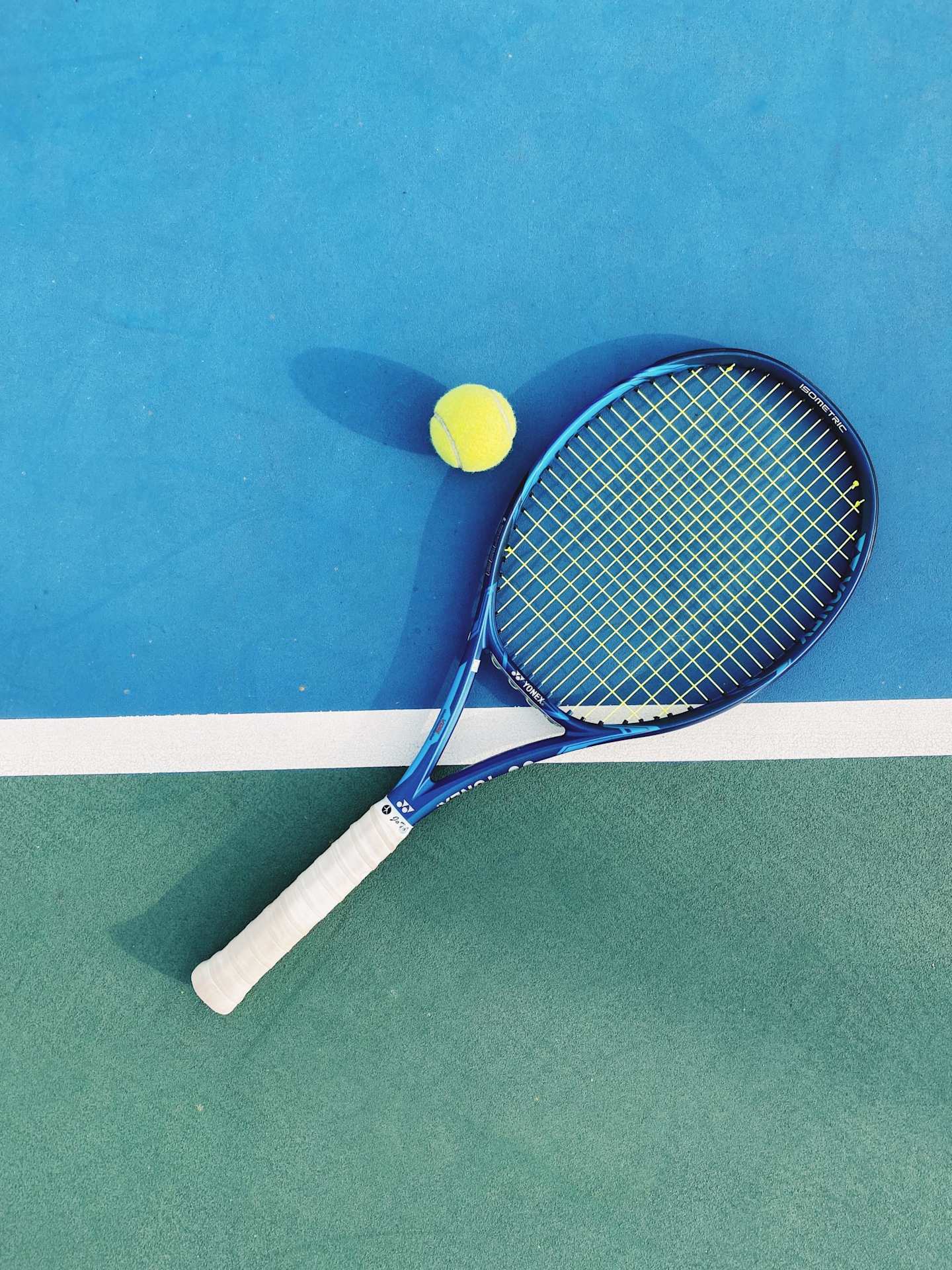 A close up view of a tennis racket and a ball on a blue and green tennis court