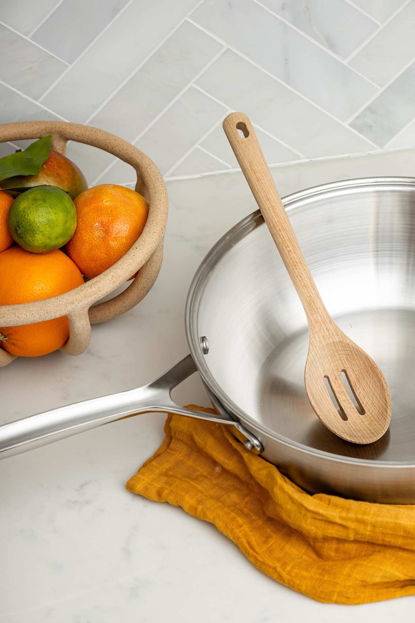A wooden spoon in a metal mixing bowl in an outdoor kitchen next to a fruit bowl