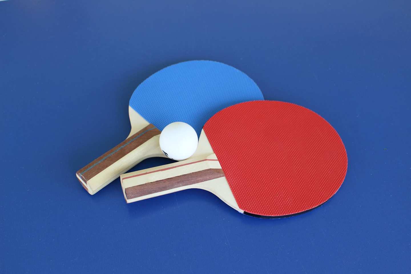 Red and blue bats on a blue table tennis table with a ball
