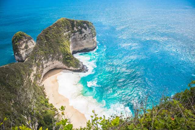 A view of the famous large, green island by the clear blue water and white sand at Kelingking Beach, Indonesia