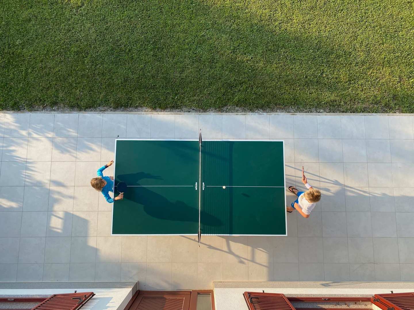 A view of two children playing table tennis in a garden from above on a sunny day