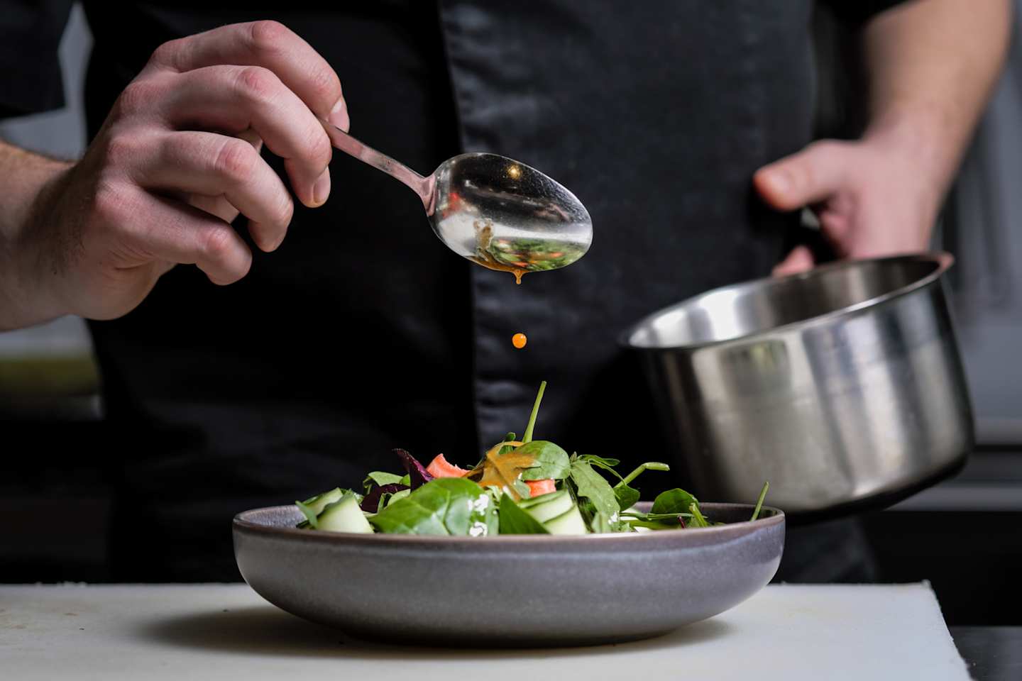 A close up of a private chef drizzling sauce onto a freshly made salad in a bowl