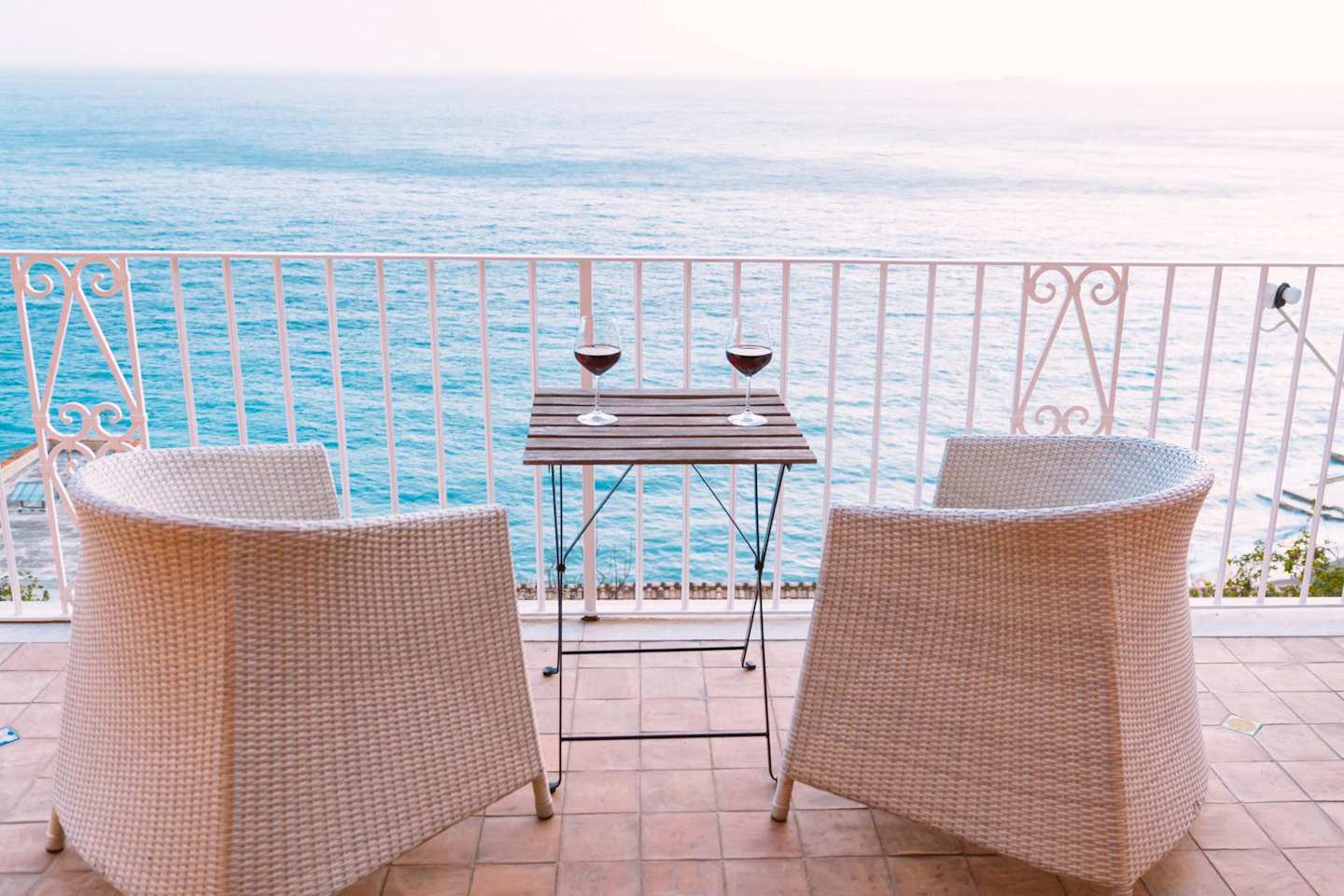 Two chairs and two glasses of red wine on a balcony overlooking the sea