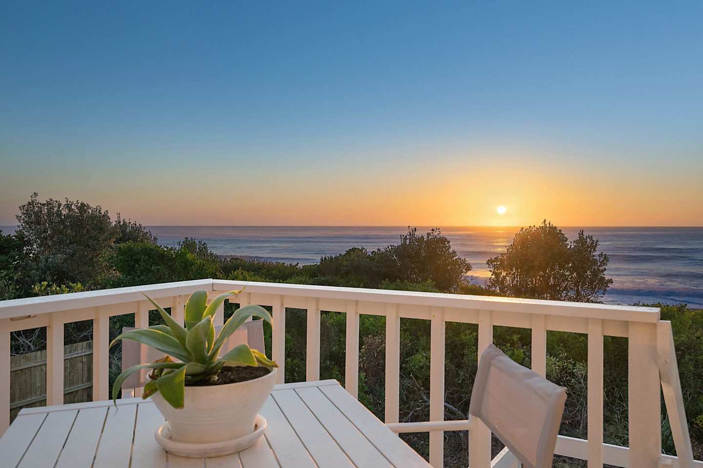 A table and chairs on a balcony overlooking the ocean at sunset