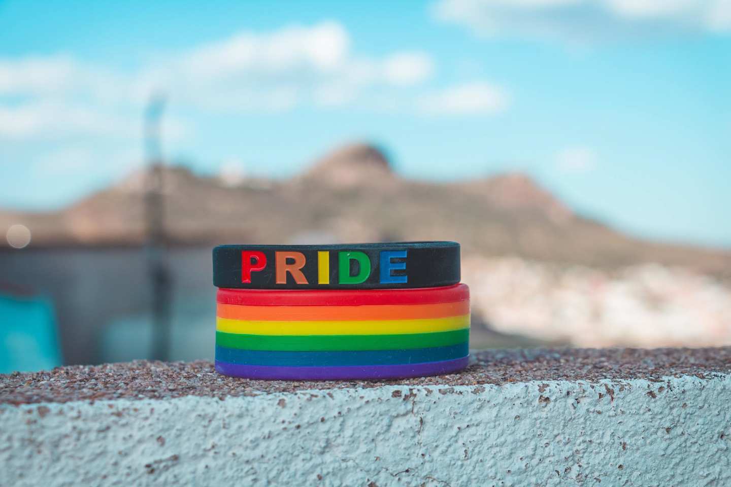 A rainbow-coloured wristband underneath a black Pride bracelet on a wall