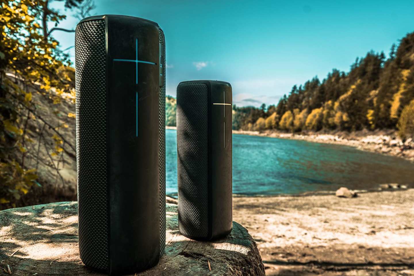 Two portable speakers outdoors in front of water in a sunny location