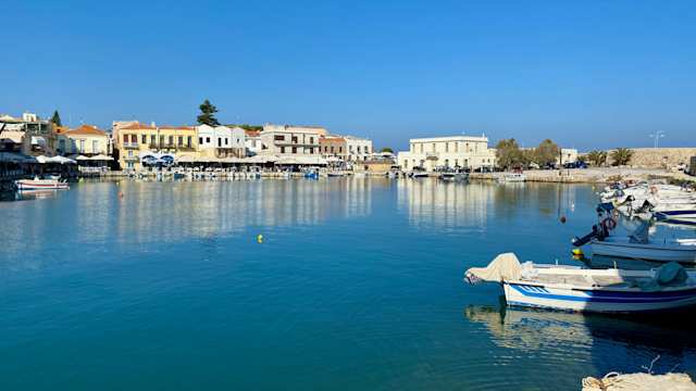 Boats docked on the blue water at a harbour in front of terraced buildings in Rethymno, Crete, Greece