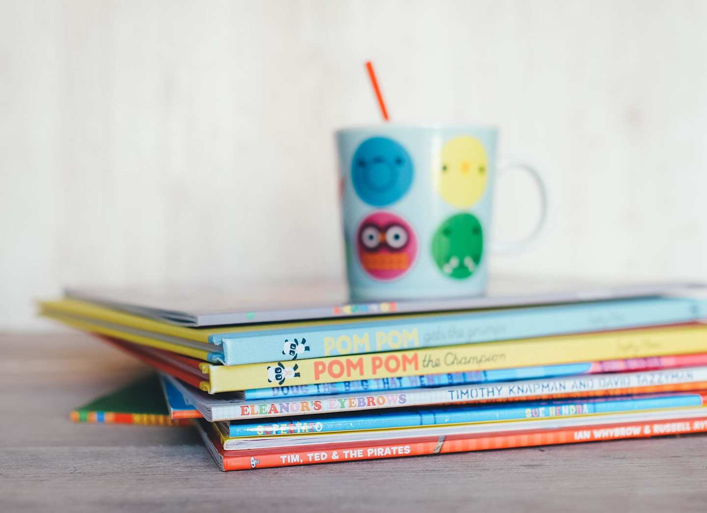 A pile of colourful children's books on a table under a mug