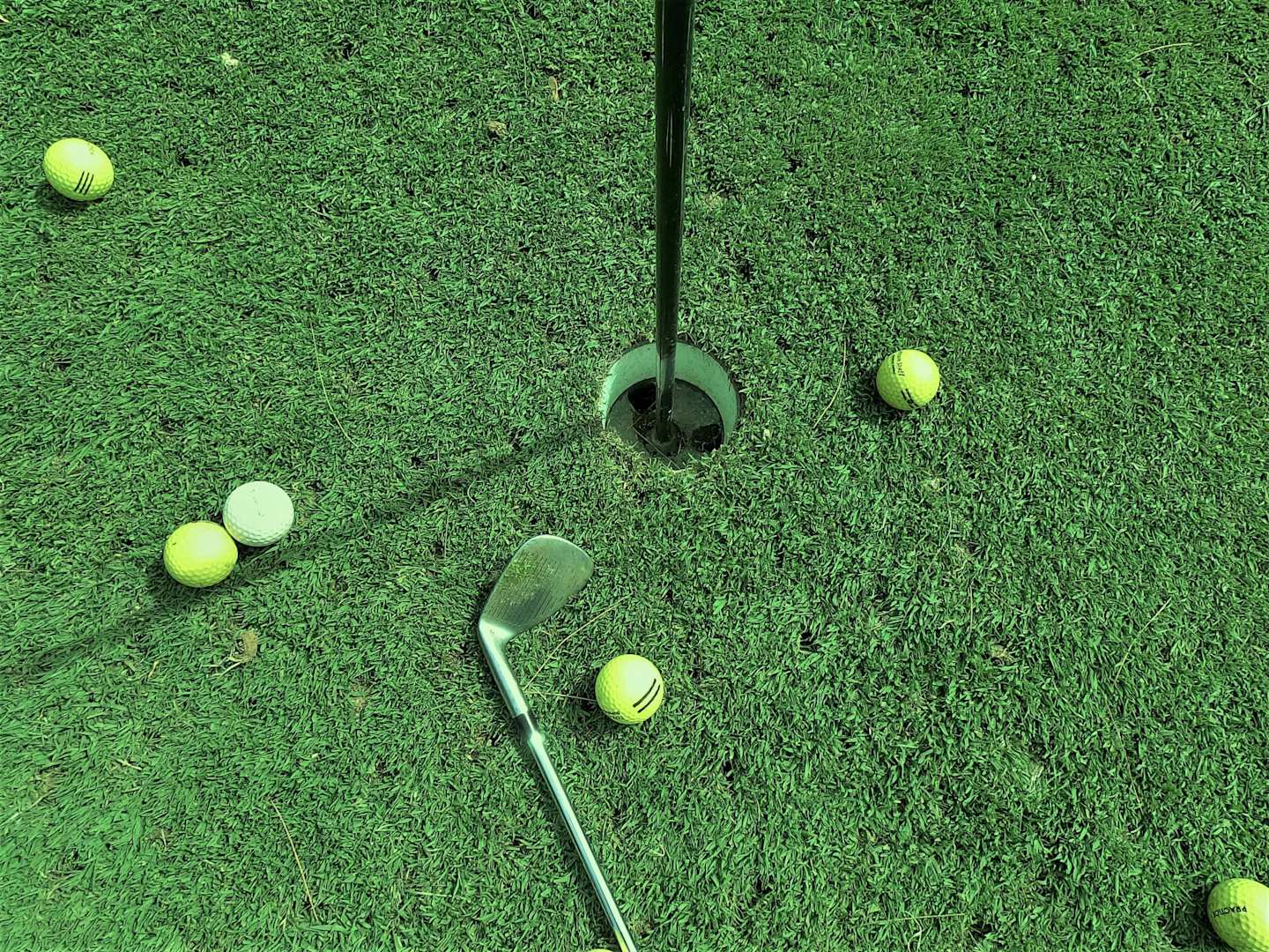 Six golf balls near hole and one golf club