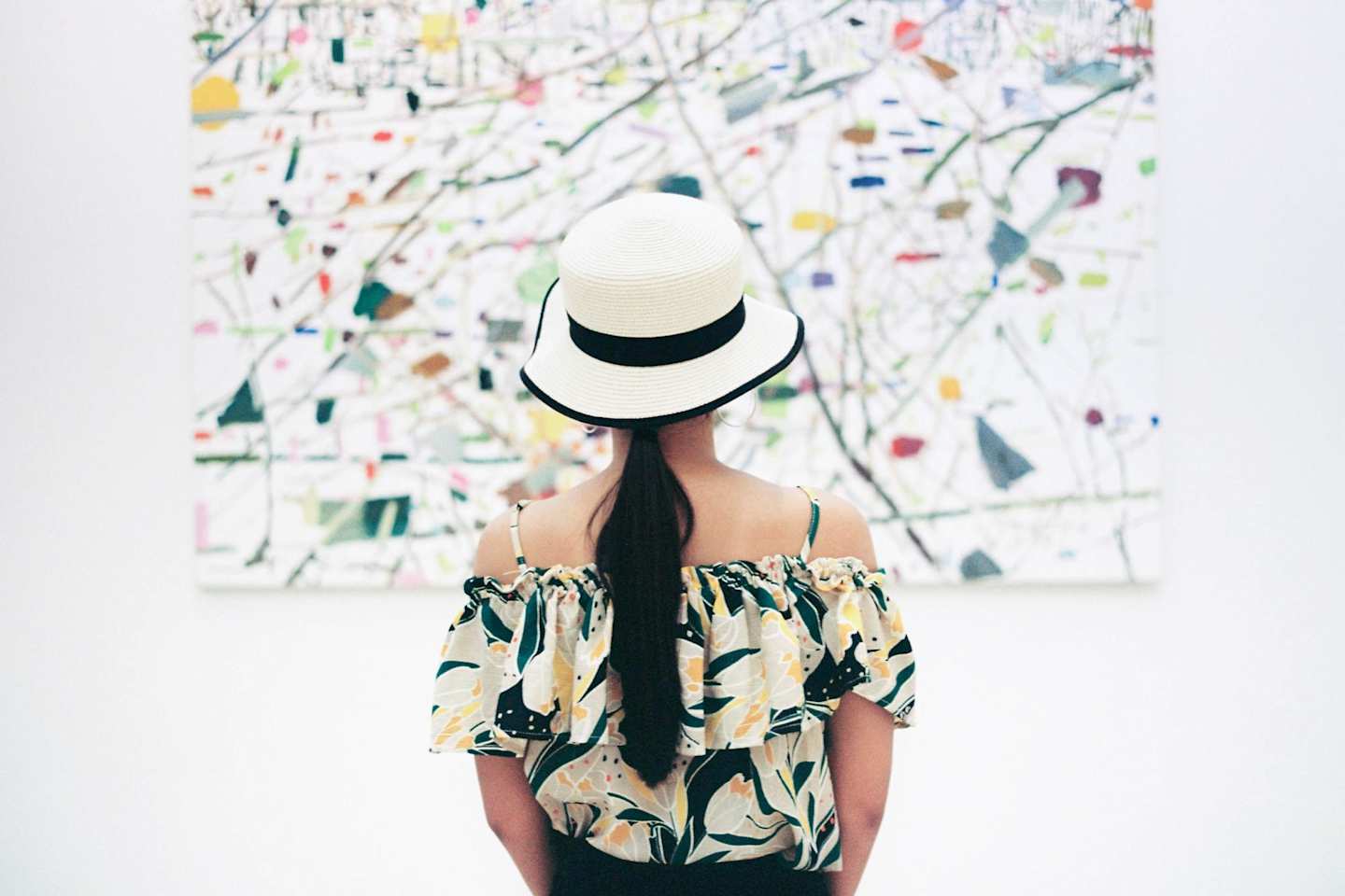 Woman in a white hat admiring abstract art work on the wall