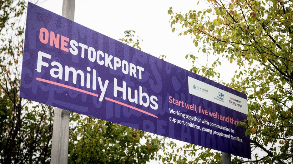A purple sign with white and pink text reads: "One Stockport Family Hubs. Start Well, live well and thrive."