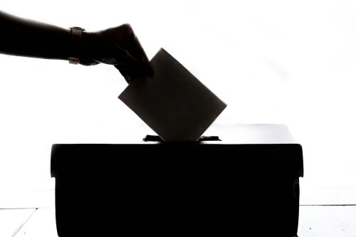 A silhouette of a hand placing a vote into a ballot box.