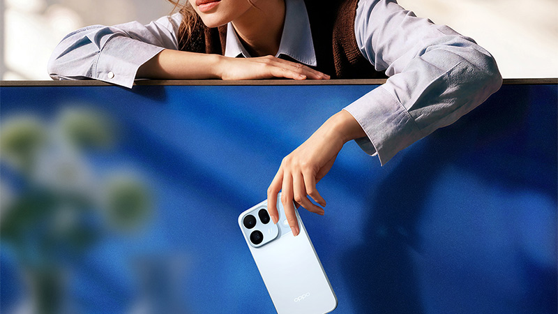 En kvinna lutar sig över en blå vägg och håller en ljusblå OPPO-smartphone med trippelkamera.