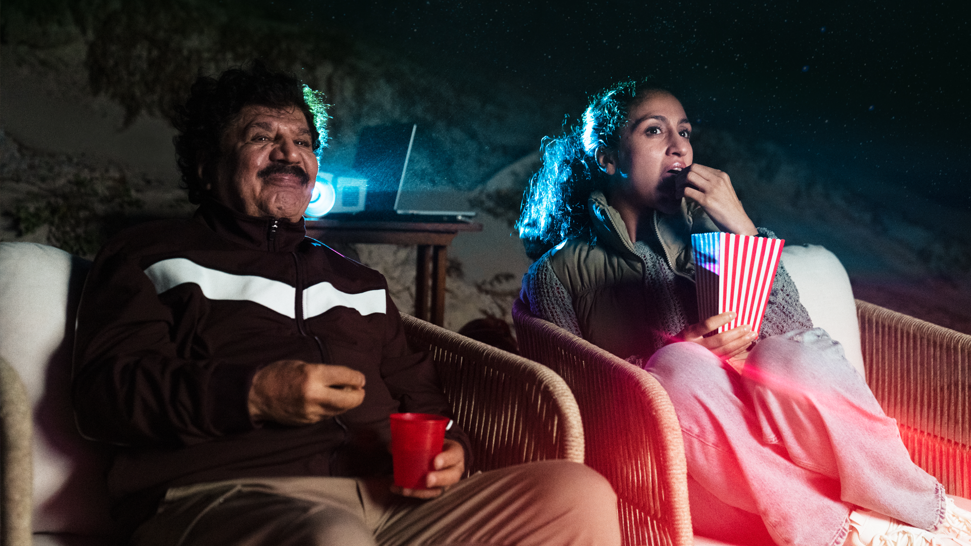Karim och Nadja sitter utomhus och kollar på film och äter popcorn.