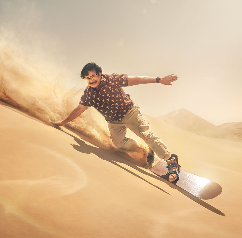 Karim surfar på sanddynor i öken, moln av sand syns efter surfbrädan