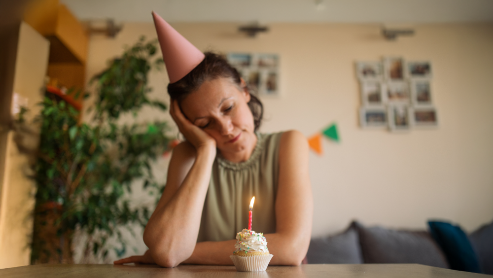 Canada's loneliness epidemic A woman with a party hat staring at a cupcake with a lit candle in it