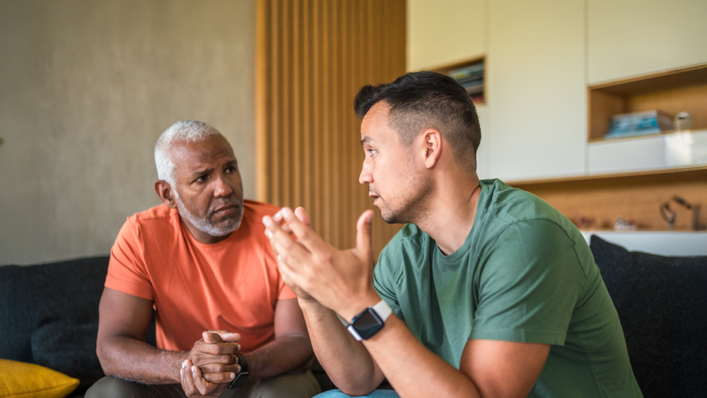Behind the mask of men's mental health Two men sitting on a couch talking with serious expressions