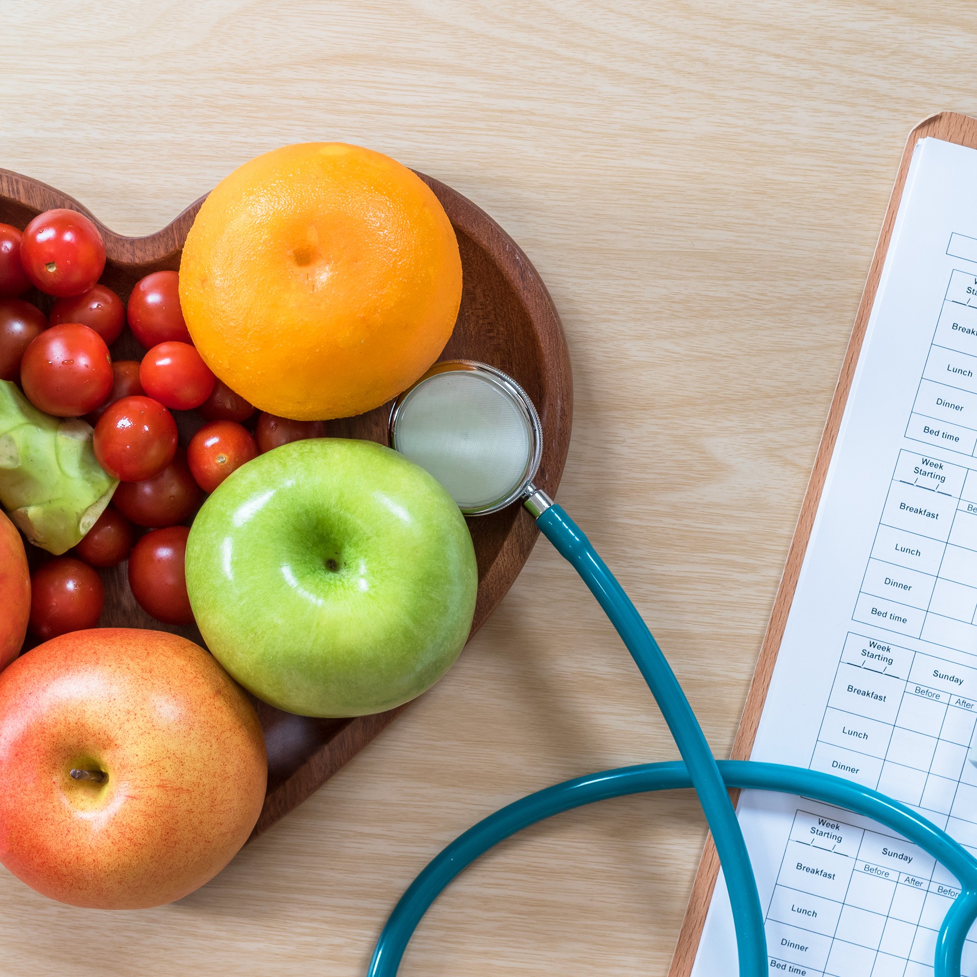 A bowl of fruit in the shape of a heart and a stethoscope with a clipboard checklist