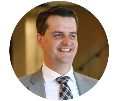 Brandon Weening headshot circle (1) Man in a suit in an office background