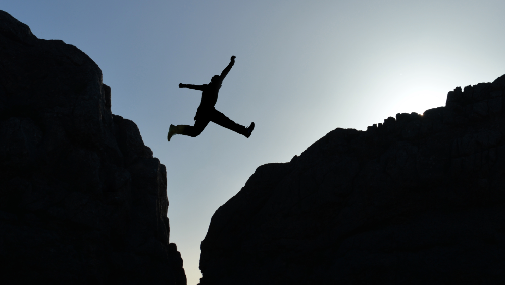Mind the gap A person jumping between two rock formations