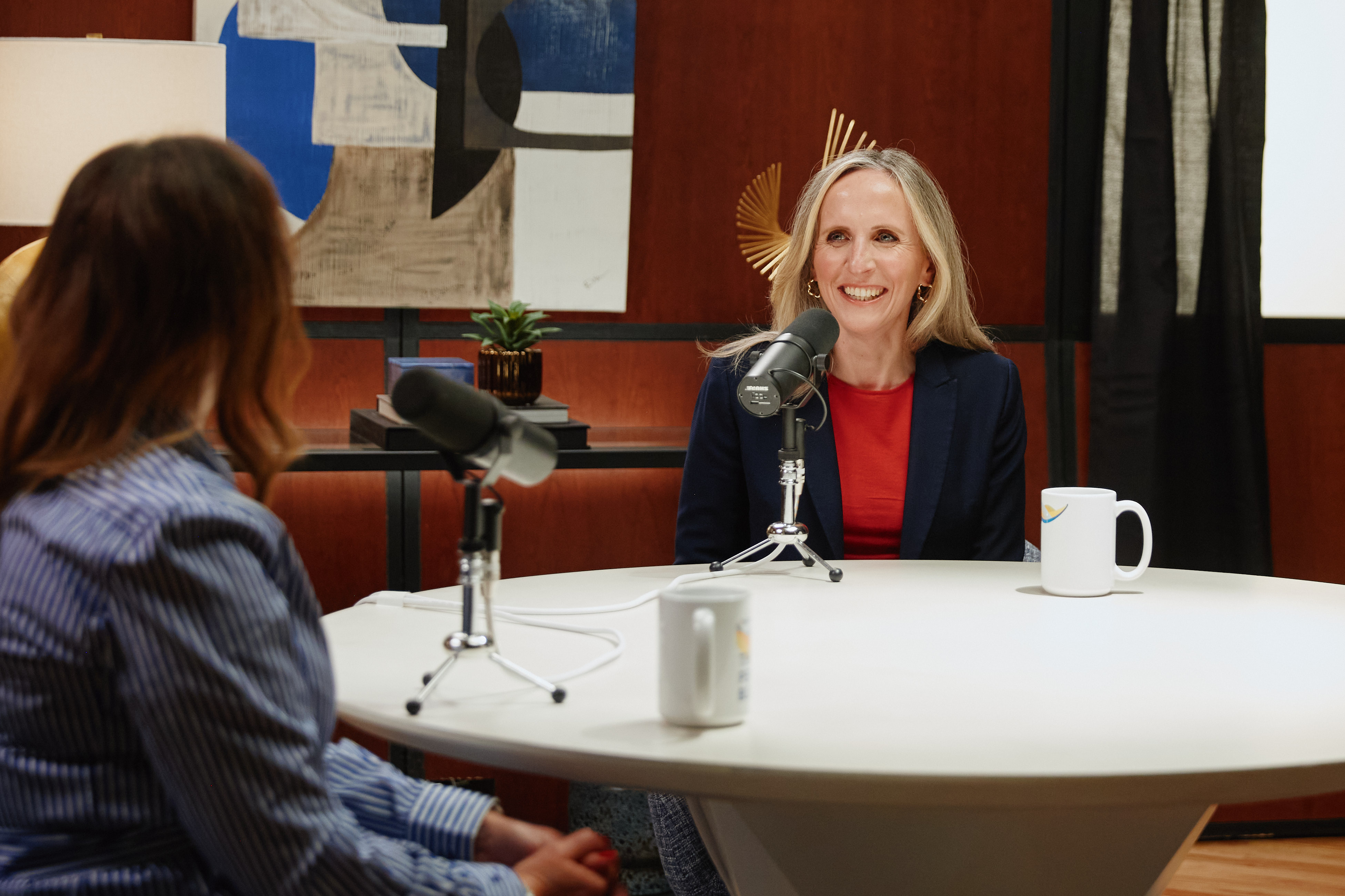 Two women sitting at a table with microphones and coffee mugs