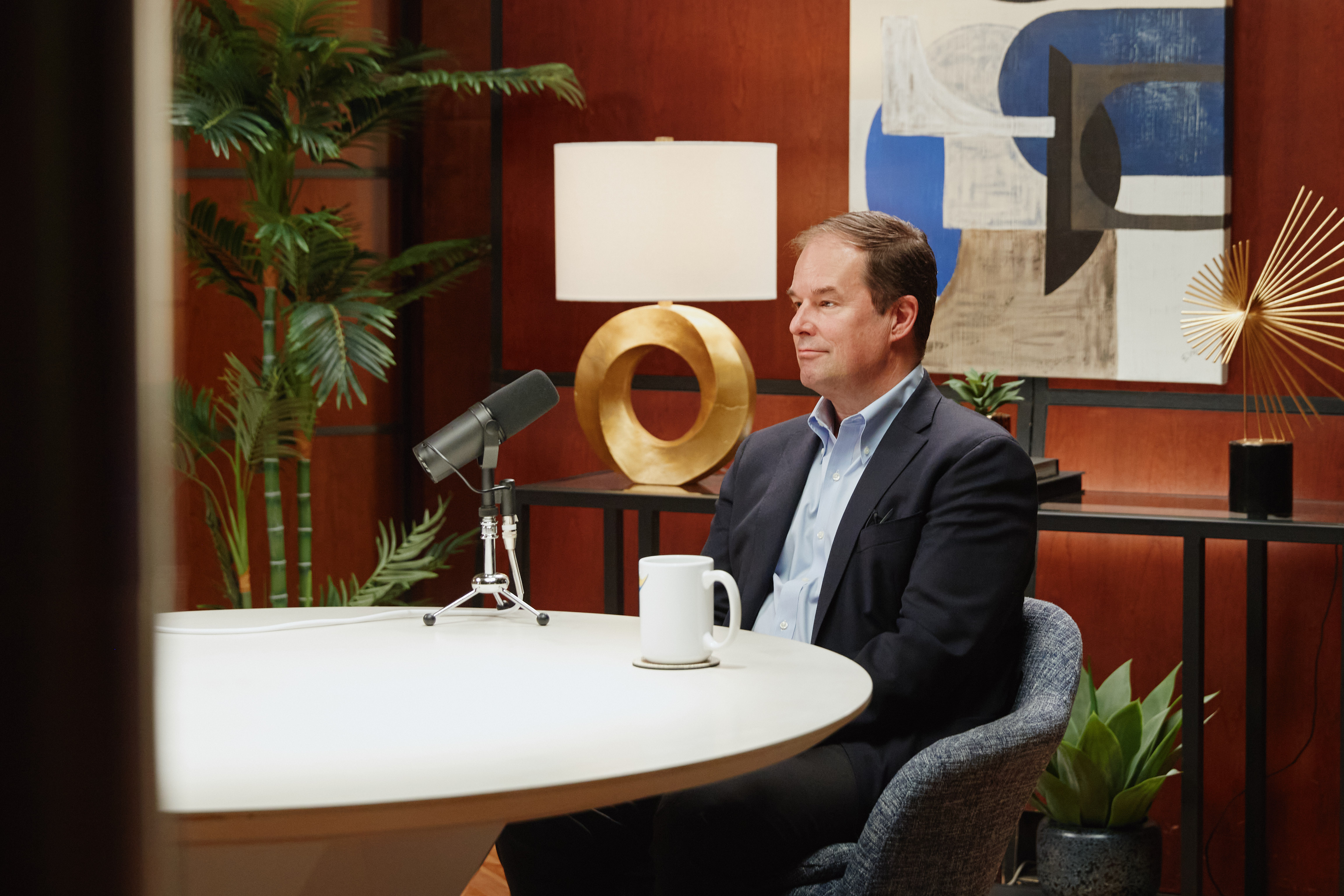 A man sitting at a table with a microphone and coffee mug