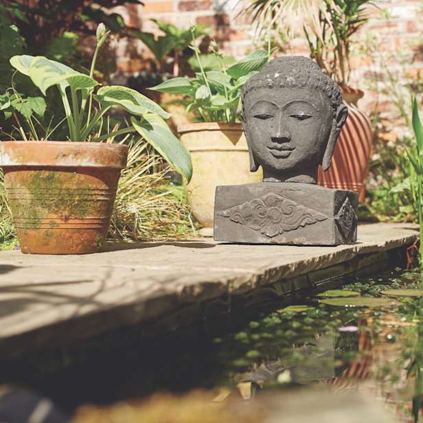 Stone buddha head on a stand in a garden next to a pond