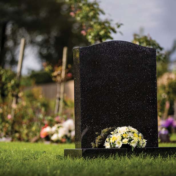 Black headstone with a white and yellow floral arrangement in a garden
