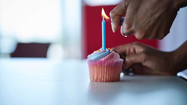 Person lighting a candle in a single cup cake.