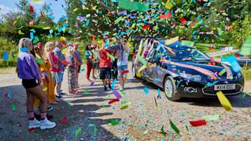 Unique tribute of a coffin being carried by mourners wearing colourful clothing and rainbow confetti being thrown.