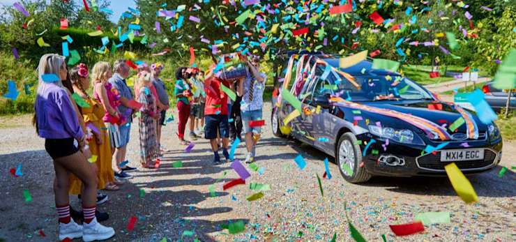 Unique tribute of a coffin being carried by mourners wearing colourful clothing and rainbow confetti being thrown.