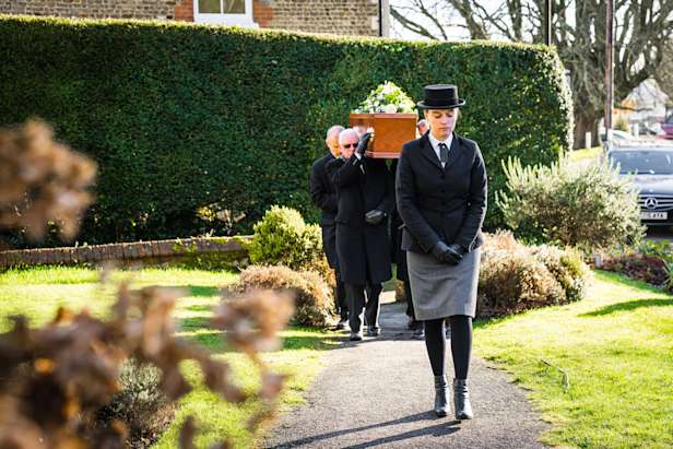 Pallbearers processing with a coffin up a path in a garden