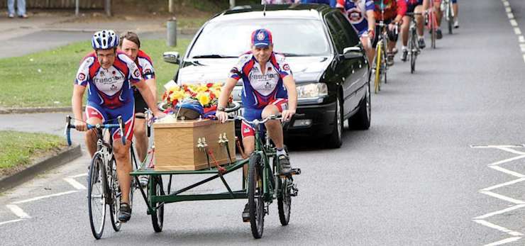 Funeral procession with a coffin with helmet and floral arrangement on a hearse pulled by bicycles