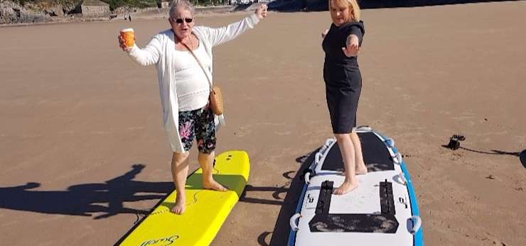 Two members of the bereavement group on surf boards on the beach.